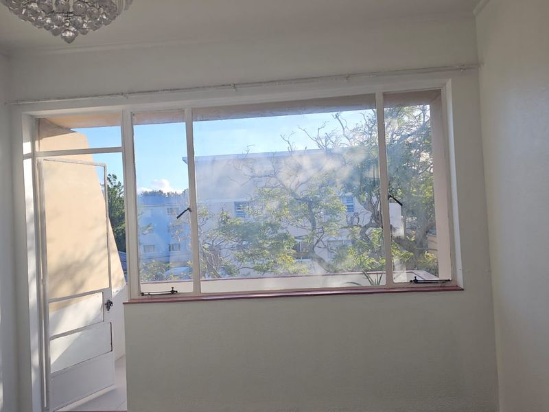 An empty living room featuring large windows, carpeted flooring, and access to an outdoor balcony area.