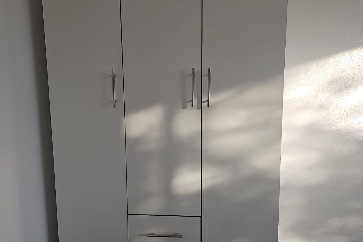 A bedroom featuring a freestanding white wardrobe with integrated drawers and metal handles.
