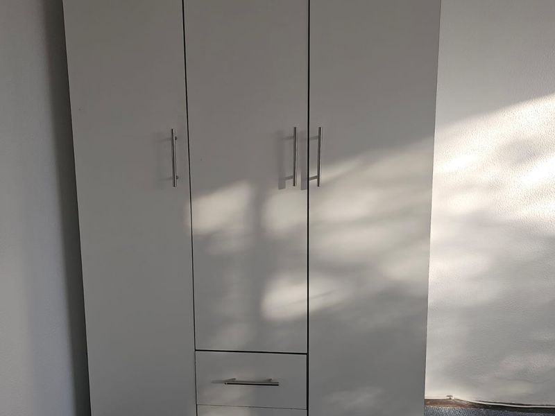 A bedroom featuring a freestanding white wardrobe with integrated drawers and metal handles.
