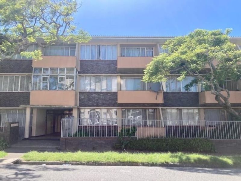 Front elevation of a multi-story apartment building featuring brick facade, private balconies, and metal perimeter fencing.