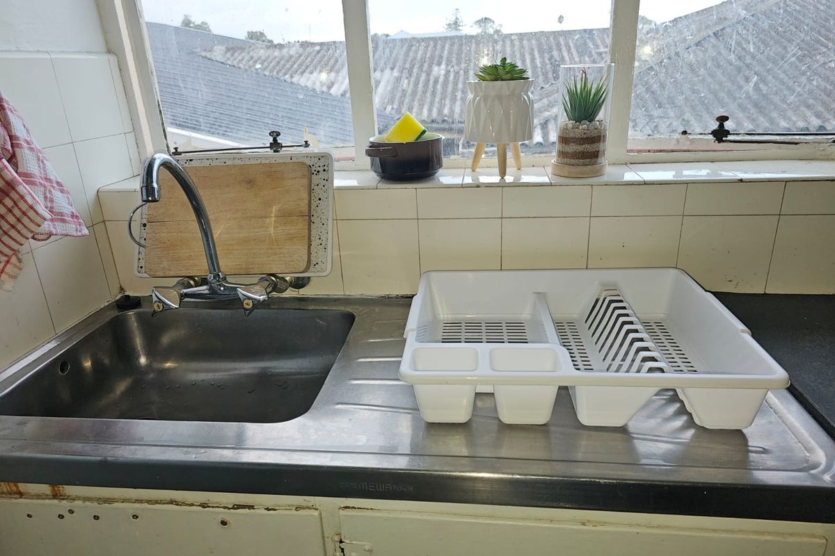 A functional kitchen sink area featuring a stainless steel basin, tiled backsplash, and built-in cabinetry, showing signs of age and wear.