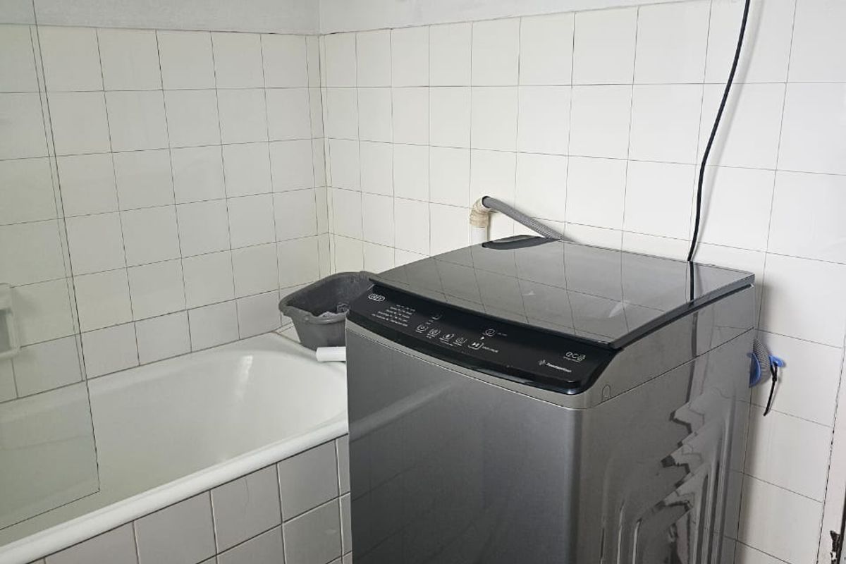 A functional bathroom featuring a built-in bathtub and tiled walls, currently utilized for laundry facilities.