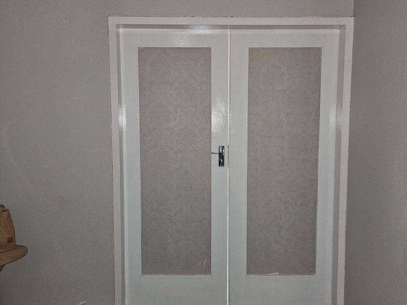 An interior view of a set of white double doors with patterned glass inserts, featuring grey carpeting and plain wall finishes.