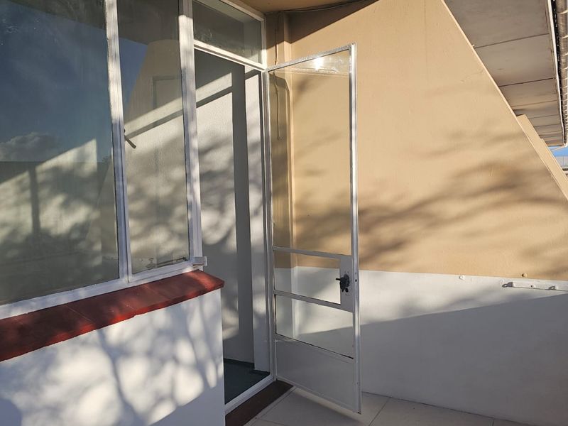 A covered balcony area featuring tiled flooring, a metal security gate, and large glass windows, offering a functional outdoor space.