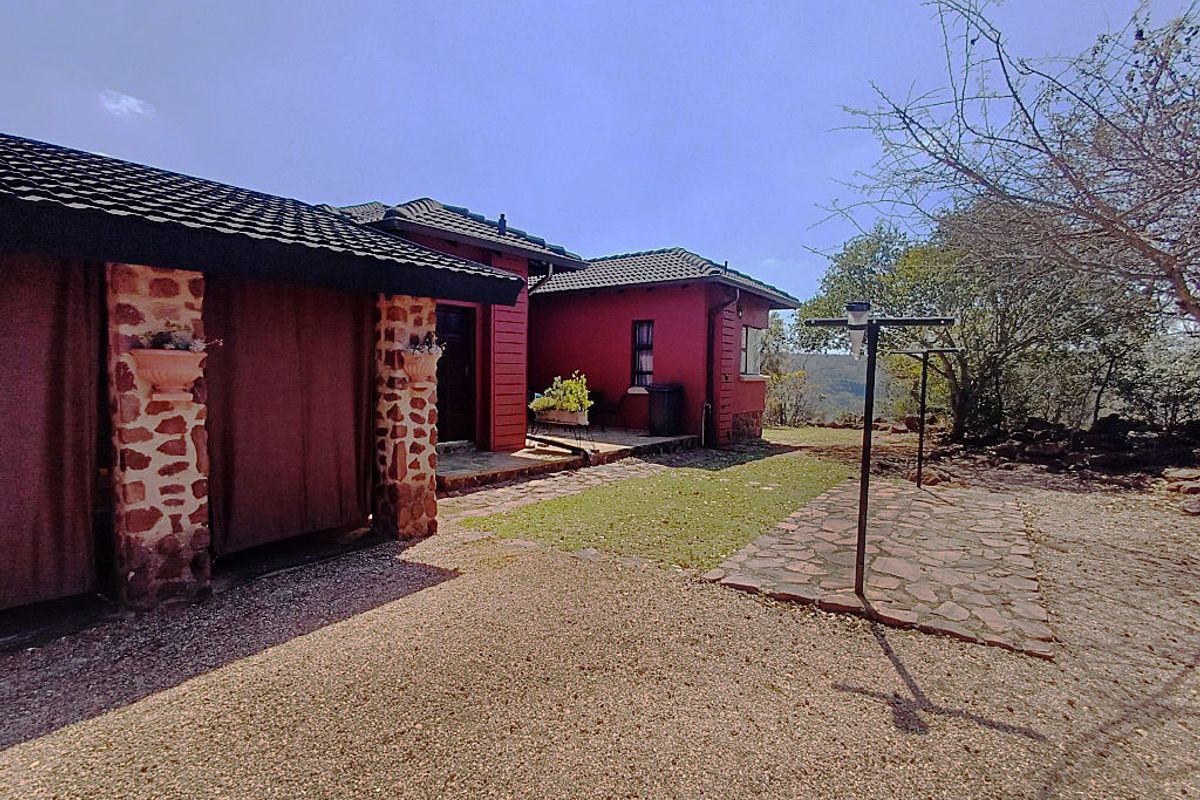 Rear view of the house featuring stone-clad pillars, a tiled roof, and a combination of paved and gravel outdoor areas.