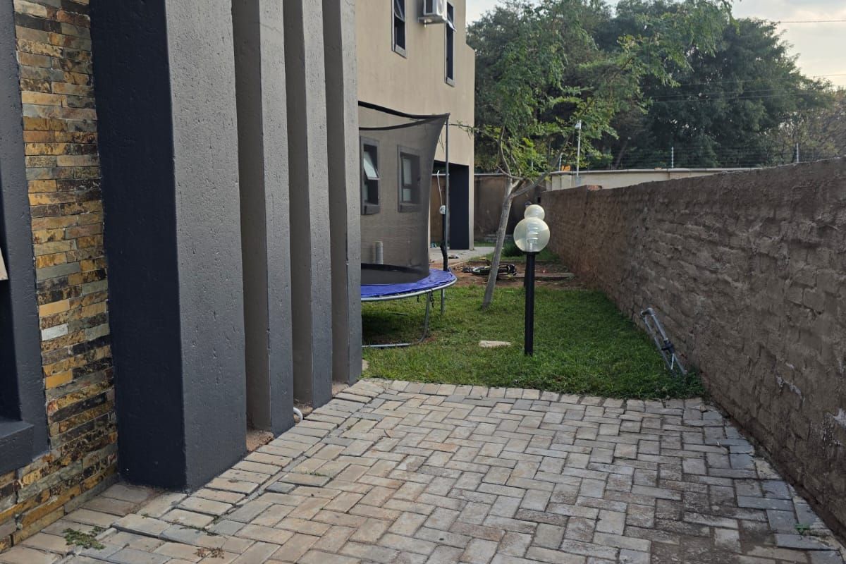 Rear exterior view featuring a paved patio area, stone-clad wall accents, and a boundary wall, providing a functional outdoor space.