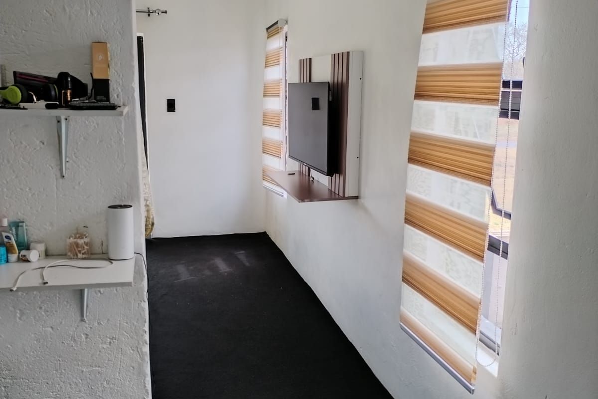 A compact bedroom featuring dark flooring, wall-mounted television unit, split-system air conditioning, and modern zebra blinds.