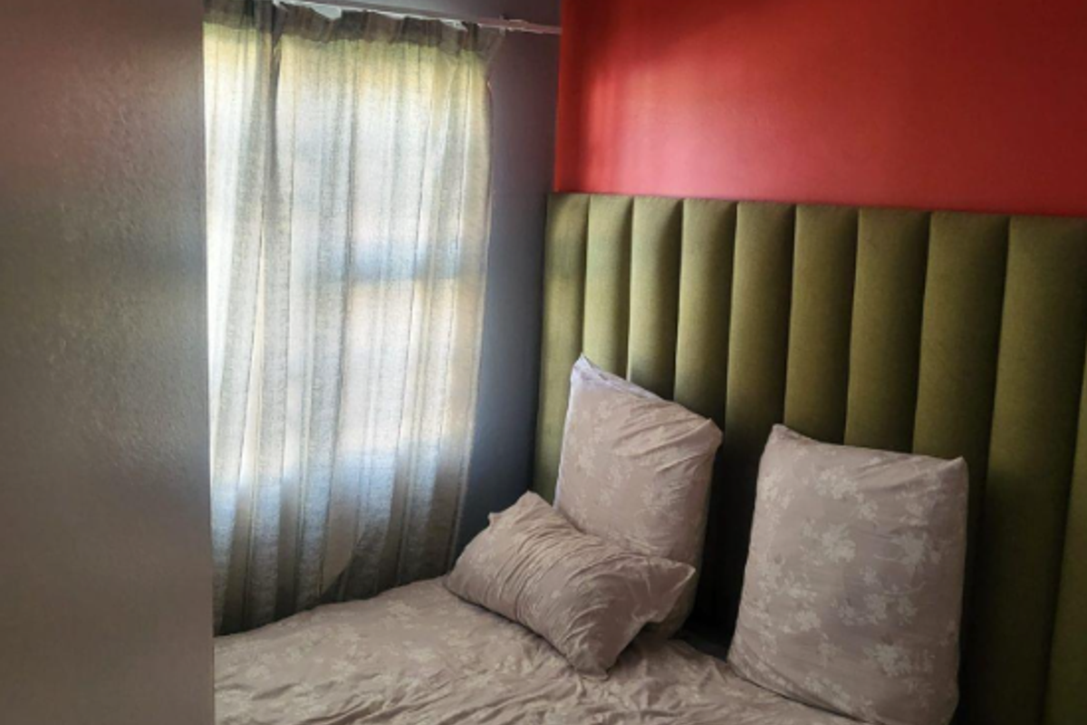 A bedroom featuring a tall upholstered headboard, a window with curtains, and painted accent walls.