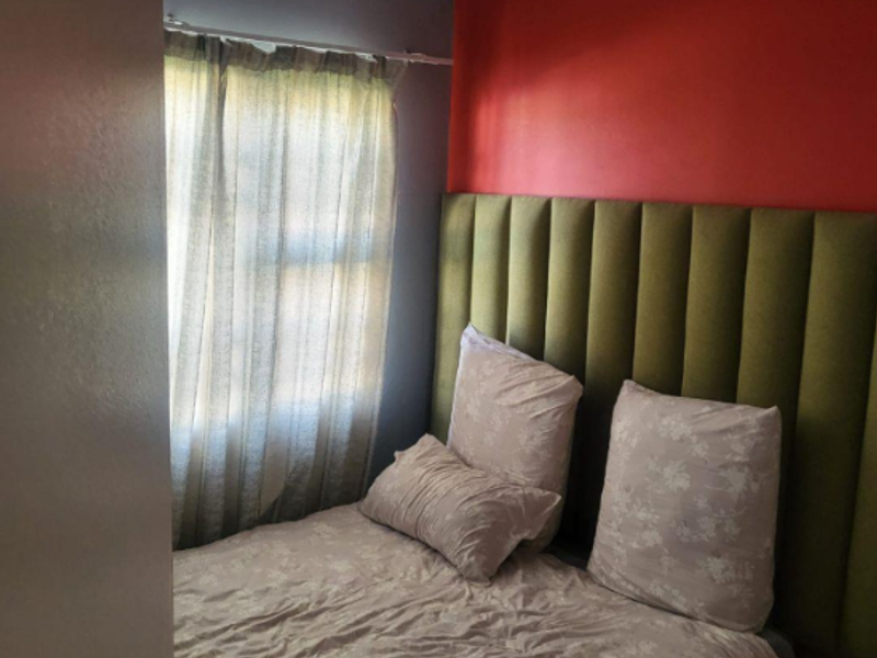 A bedroom featuring a tall upholstered headboard, a window with curtains, and painted accent walls.