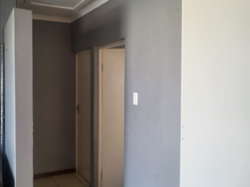 A simple, empty hallway featuring tiled flooring, neutral grey and white walls, and access to internal rooms via standard doors.