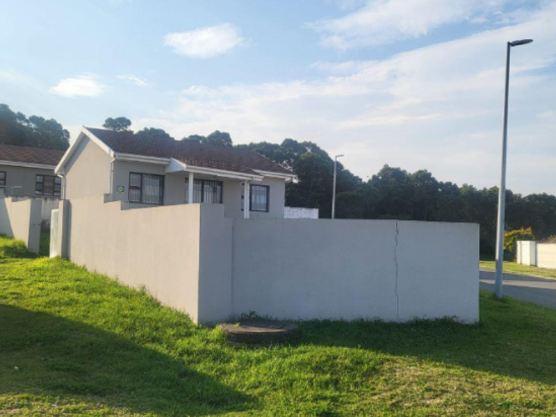 A view of the front exterior of the house featuring a perimeter wall with a visible crack and a tiled roof.