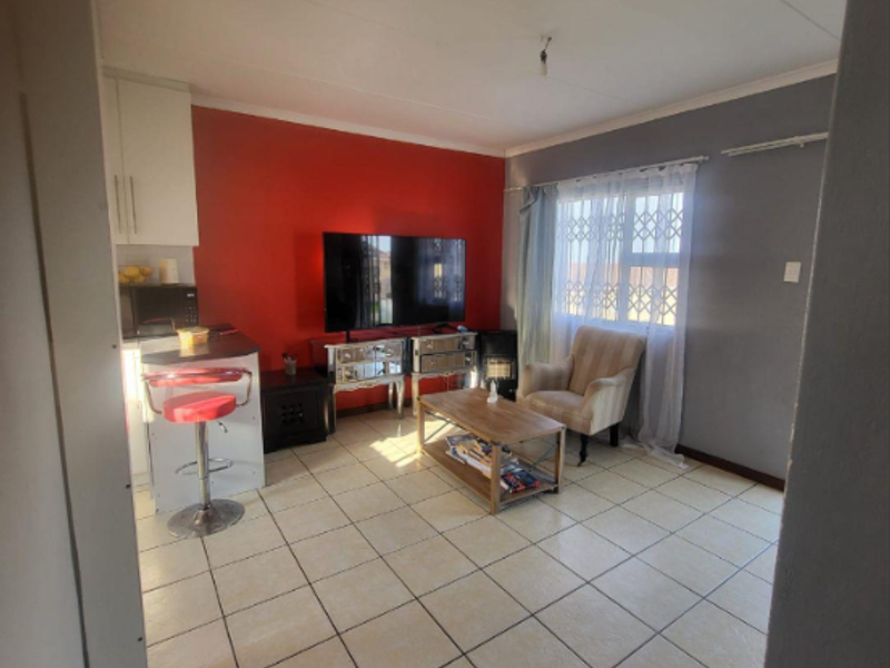 Open-plan living area featuring tiled flooring, a security gate on the window, and integrated kitchen cabinetry.