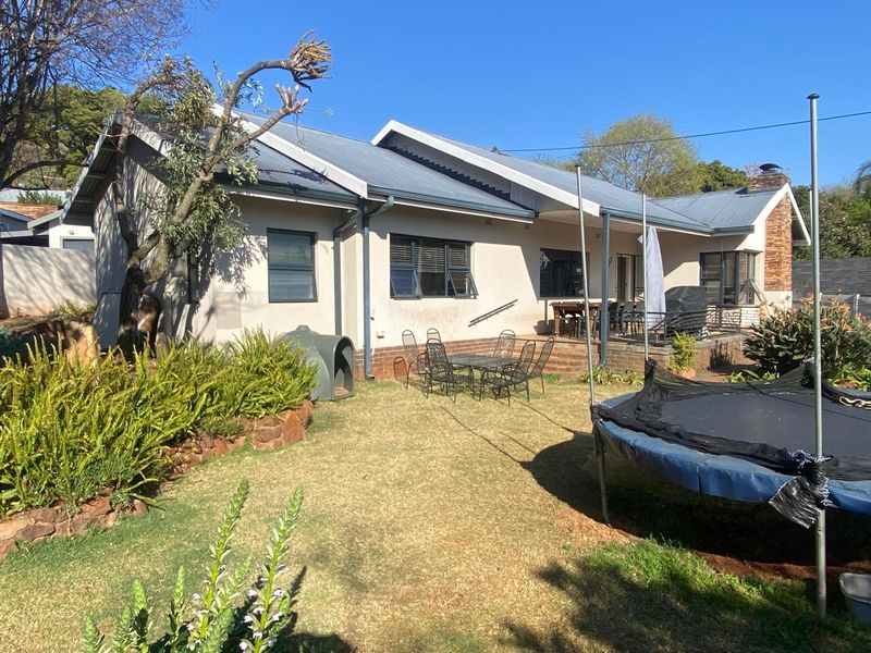 Rear view of the house featuring a paved patio area, corrugated metal roofing, and a landscaped garden.