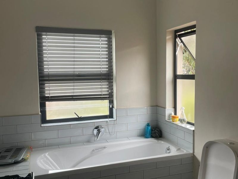 A clean and functional bathroom featuring a built-in bathtub with subway tile surround, a modern toilet, and natural light from dual windows.