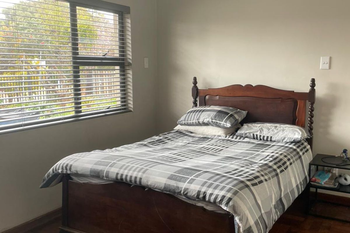 A bedroom featuring classic parquet flooring, neutral wall finishes, and a large window fitted with venetian blinds, providing natural light.