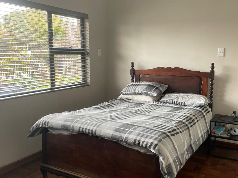 A bedroom featuring classic parquet flooring, neutral wall finishes, and a large window fitted with venetian blinds, providing natural light.