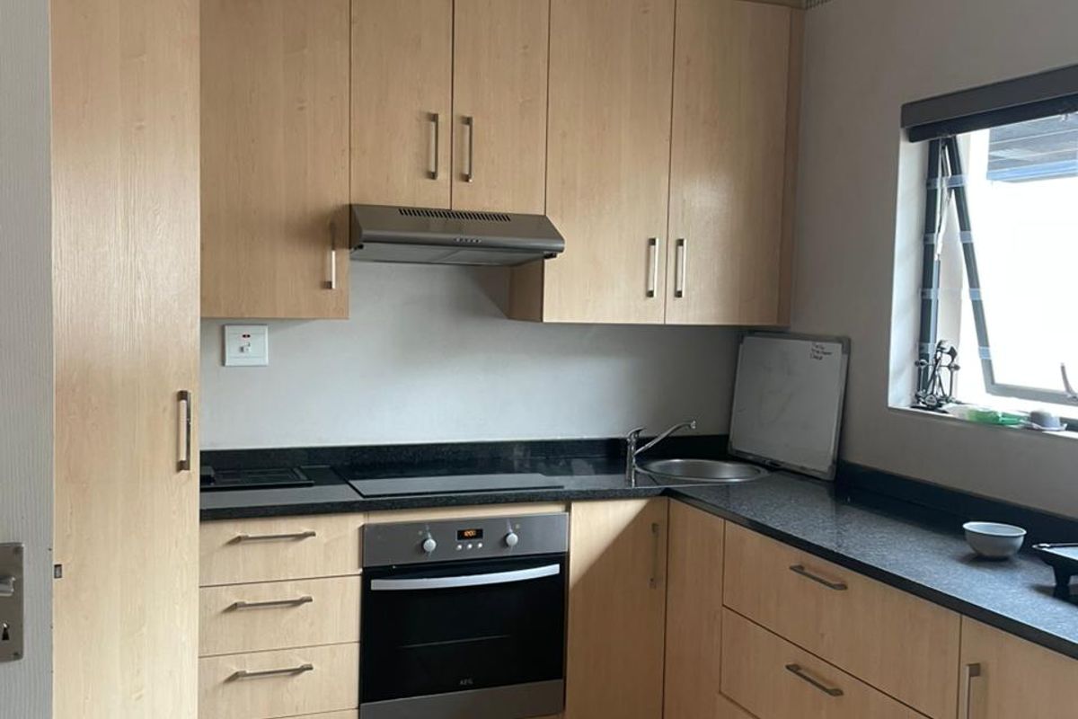 A functional kitchen featuring light wood cabinetry, dark laminate countertops, built-in oven and hob, and tiled flooring.