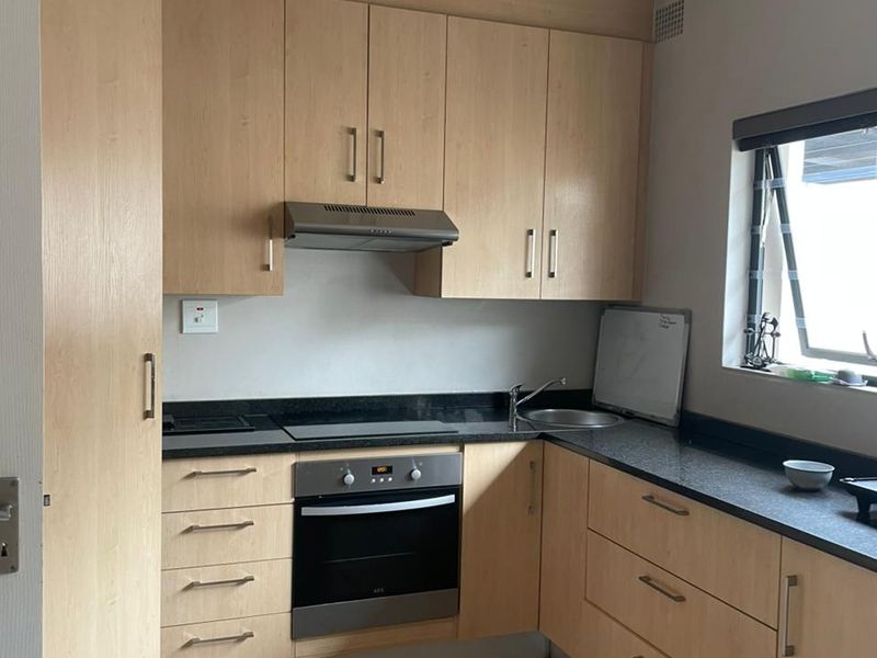 A functional kitchen featuring light wood cabinetry, dark laminate countertops, built-in oven and hob, and tiled flooring.