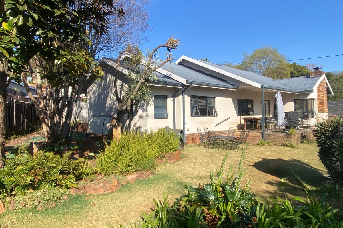 Rear view of the house featuring a covered patio area, established garden with stone retaining walls, and a corrugated metal roof.