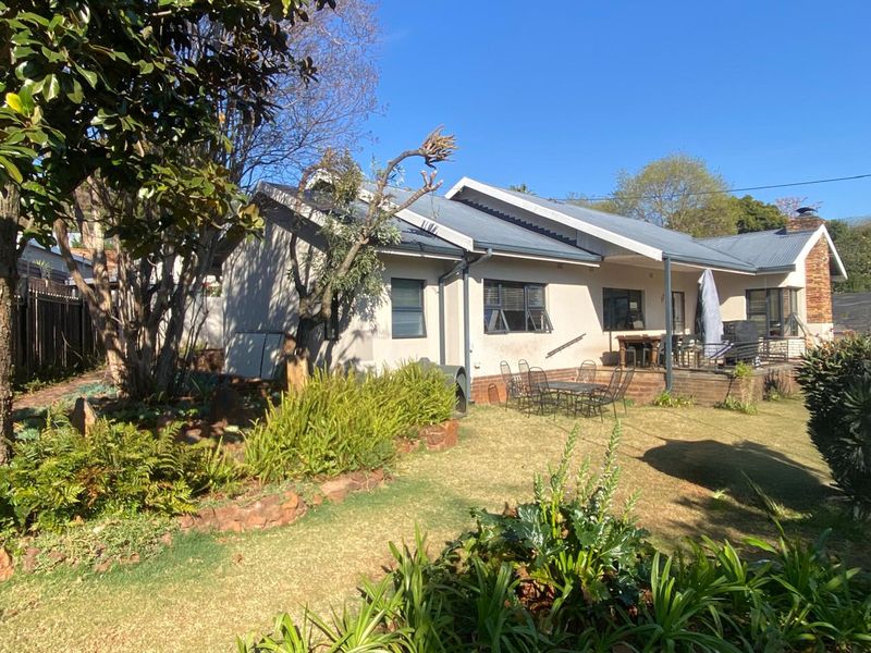 Rear view of the house featuring a covered patio area, established garden with stone retaining walls, and a corrugated metal roof.