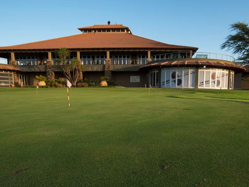 A view of the clubhouse building featuring a terracotta tile roof, stone accents, and a well-maintained putting green in the foreground.