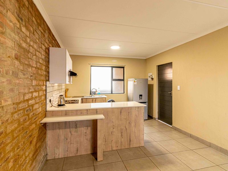A functional kitchen featuring an exposed brick feature wall, modern cabinetry, stone countertops, a breakfast bar, and tiled flooring.