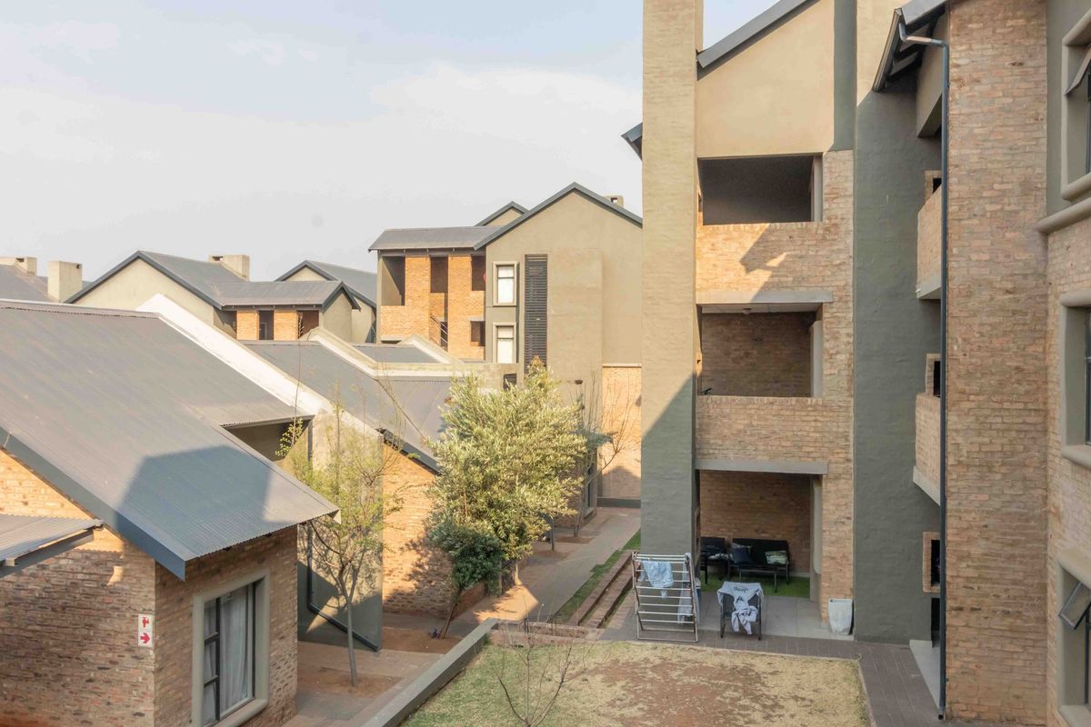 An elevated view of a townhouse complex featuring brick facades, corrugated metal roofing, and shared outdoor walkways between residential units.