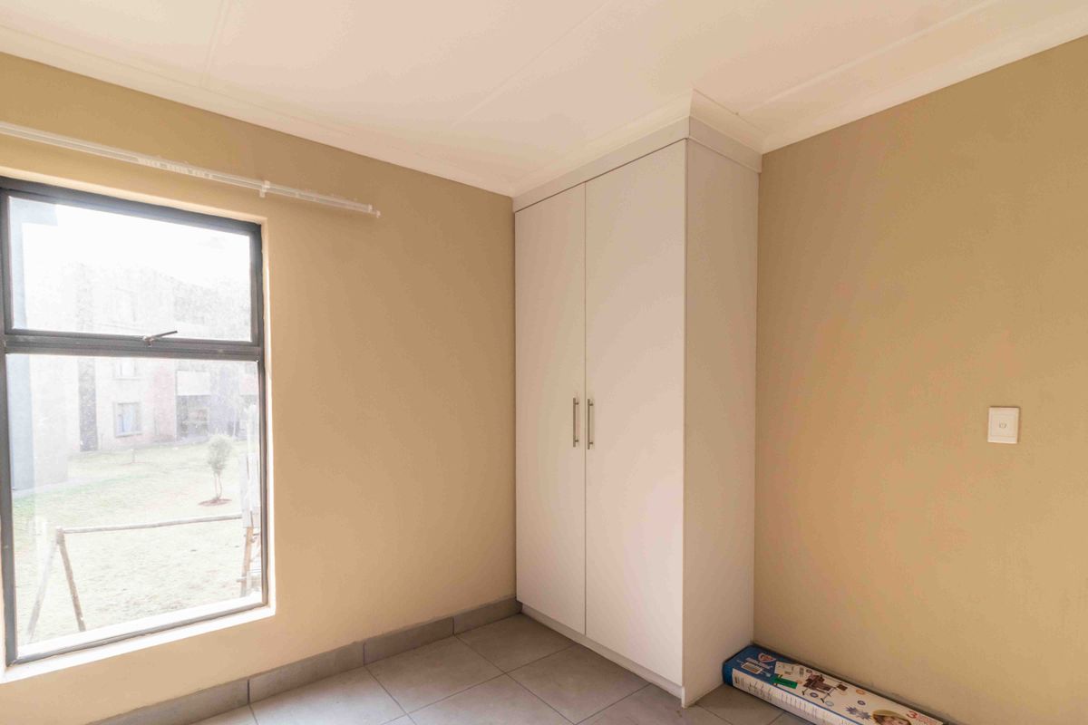 A clean, empty bedroom featuring neutral wall paint, tiled flooring, and a built-in wardrobe with white cabinetry.