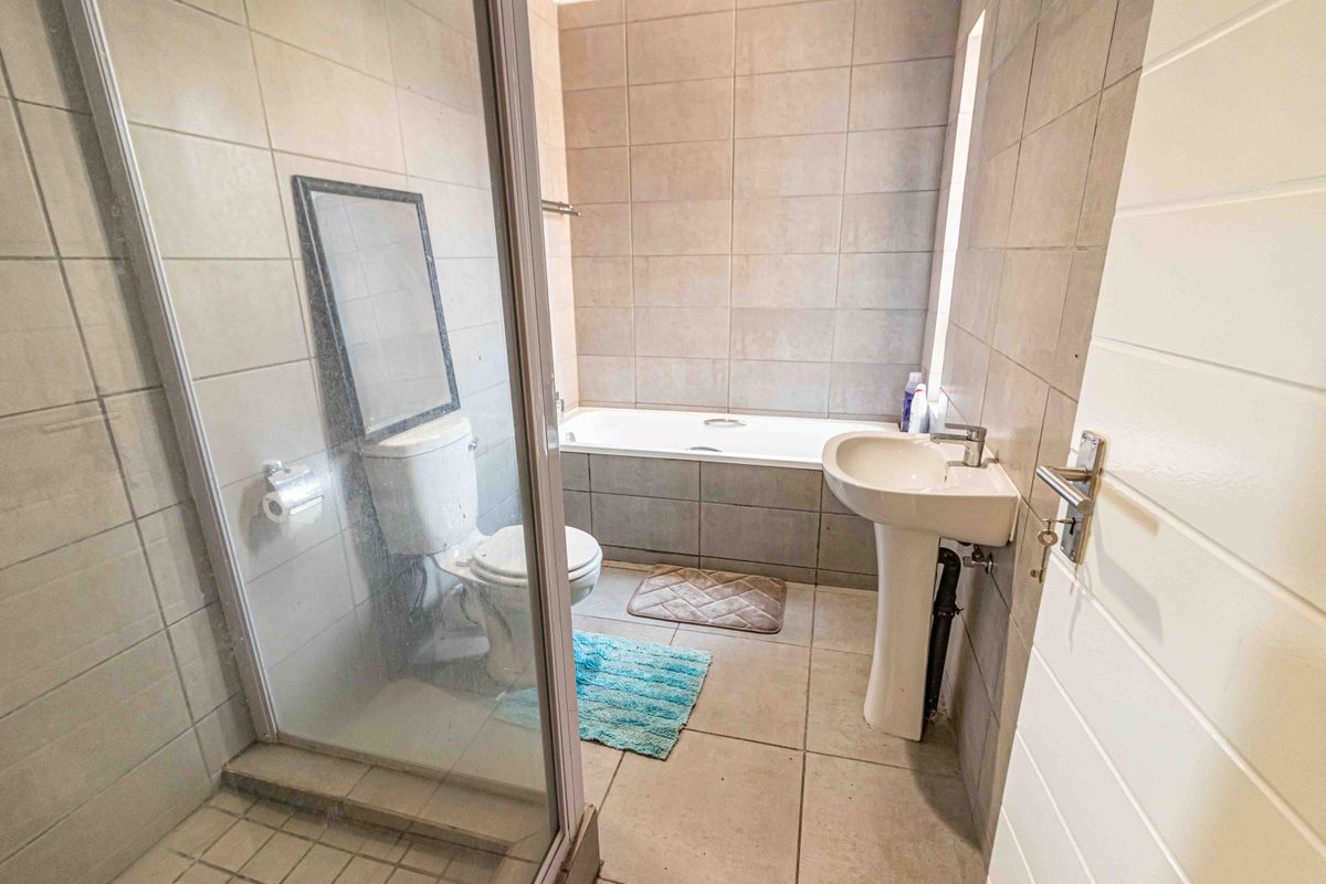 A functional bathroom featuring a shower enclosure, bathtub, pedestal basin, and toilet with neutral wall and floor tiling.