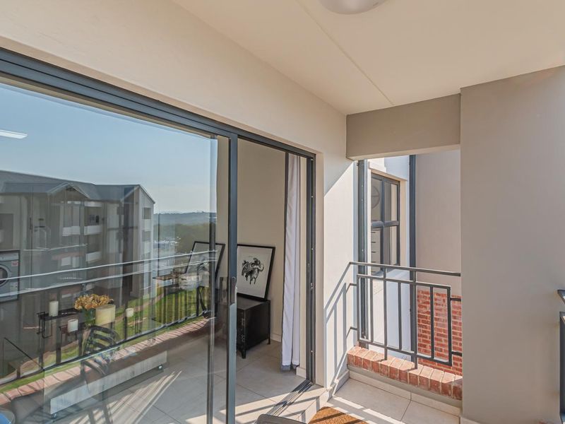 A clean, modern balcony featuring tiled flooring, a metal safety railing with brick detailing, and large sliding glass doors leading into the apartment.