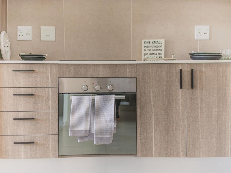 Modern kitchen featuring light wood-grain cabinetry, stone countertops, a tiled backsplash, and a built-in Bosch oven with integrated hob.