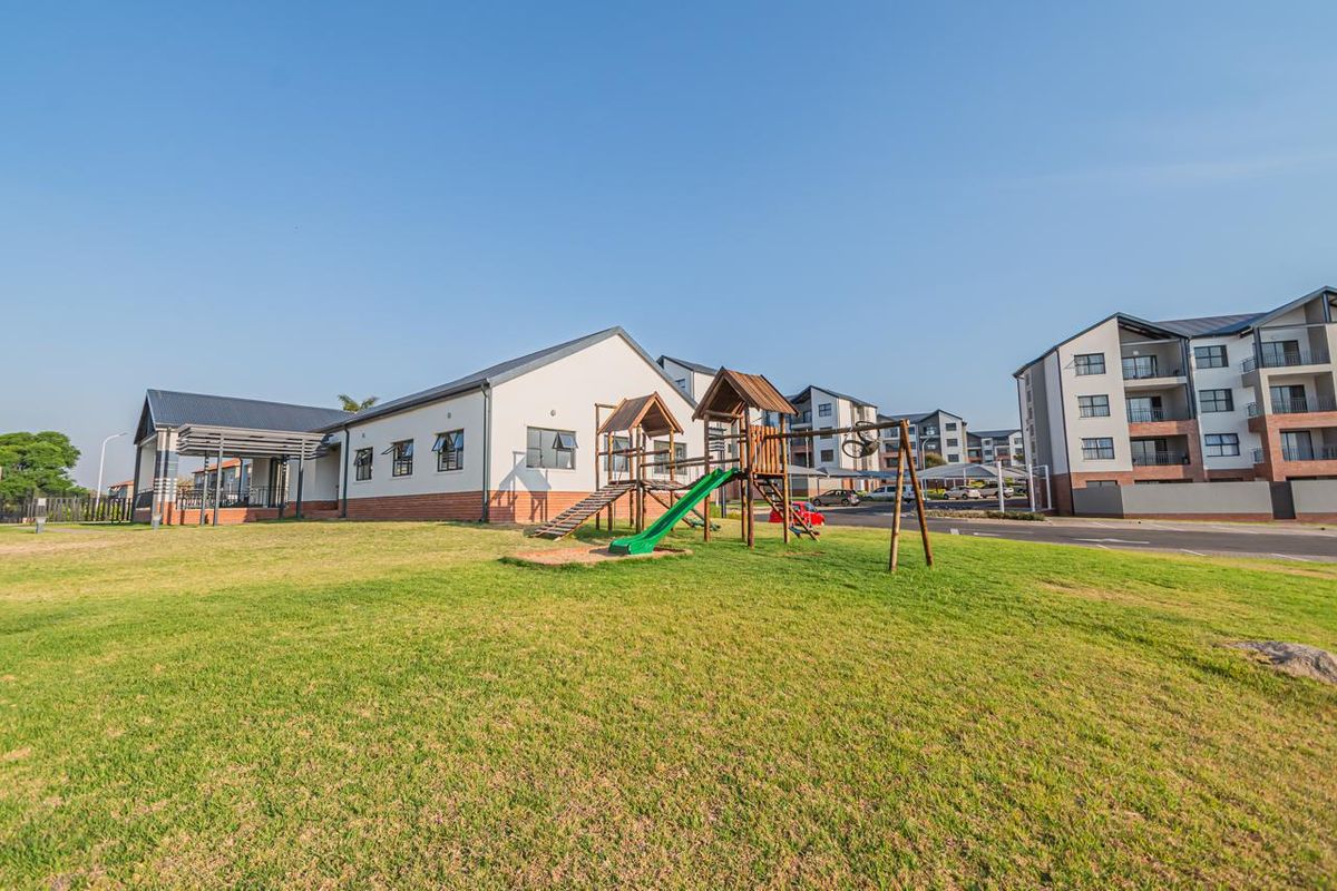 A view of the apartment complex grounds featuring a well-maintained lawn and a children's playground area.