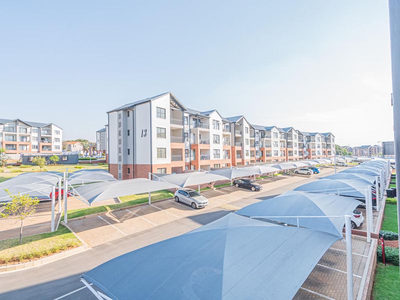 Exterior view of a modern apartment complex featuring multiple blocks, paved parking areas, and shade cloth carports for residents.
