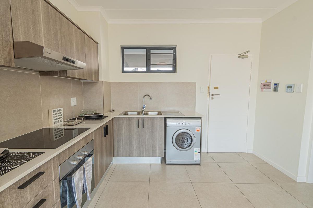 Modern kitchen featuring wood-look cabinetry, integrated electric hob and oven, stainless steel sink, and tiled flooring with a neutral backsplash.