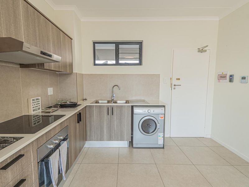 Modern kitchen featuring wood-look cabinetry, integrated electric hob and oven, stainless steel sink, and tiled flooring with a neutral backsplash.