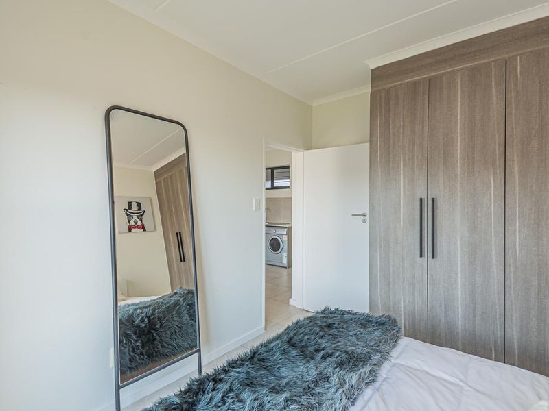 A well-maintained bedroom featuring modern built-in wardrobes with wood-grain finish and coving, with a view into an adjacent laundry area.