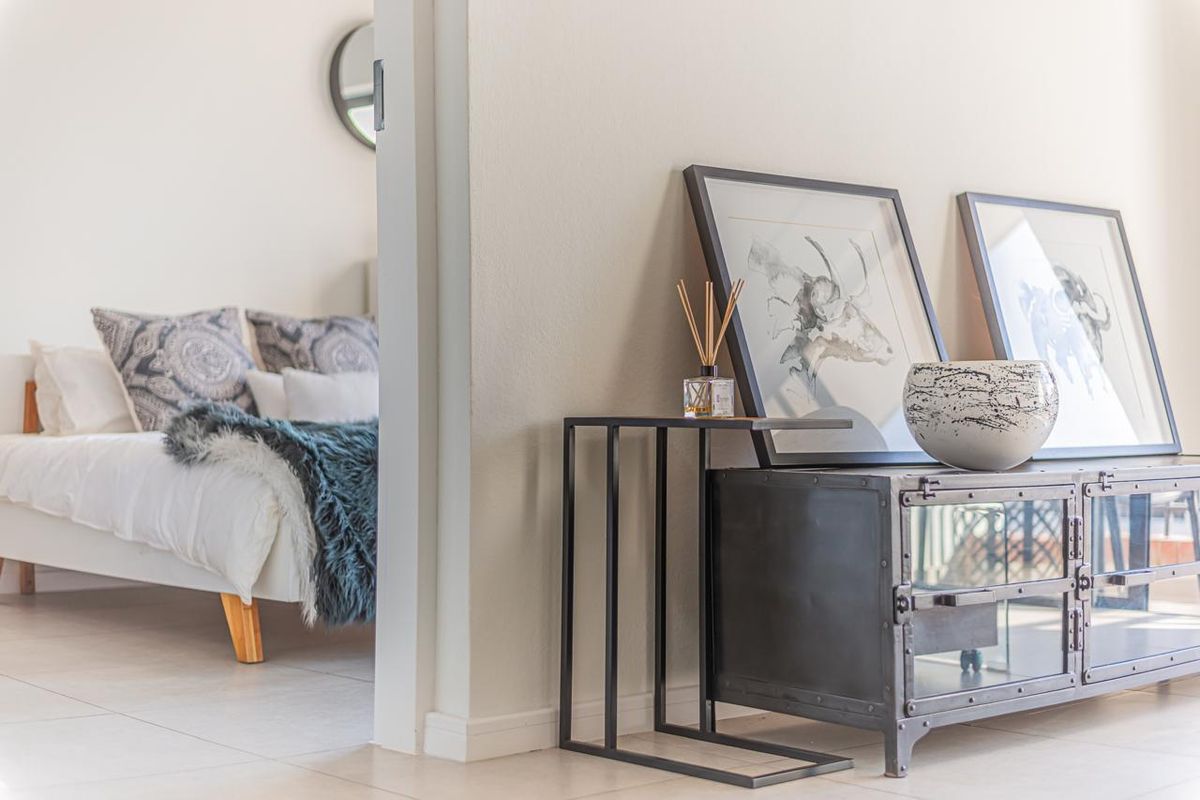 A bright bedroom interior featuring neutral wall finishes and clean tiled flooring, viewed through an open doorway from an adjacent living space.