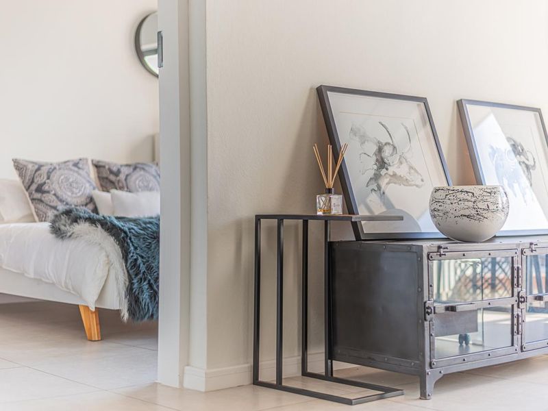 A bright bedroom interior featuring neutral wall finishes and clean tiled flooring, viewed through an open doorway from an adjacent living space.