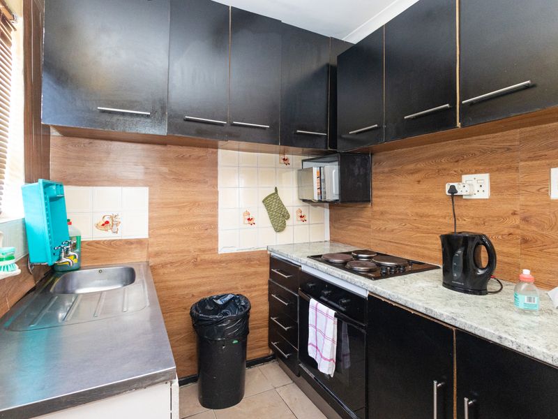 Compact kitchen featuring black cabinetry, wood-look splashback, stainless steel sink, and built-in electric oven and hob with stone-look laminate countertops.