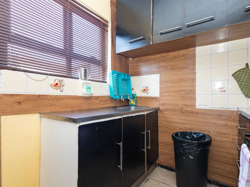 A compact kitchen area featuring built-in cabinetry, a stainless steel sink, and tiled backsplash with wood-look wall paneling.