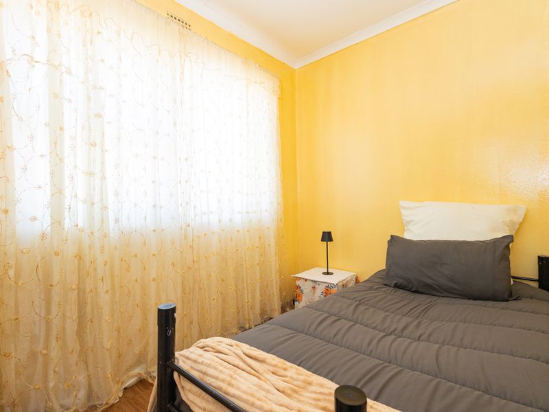 A bedroom featuring yellow painted walls, laminate flooring, and a large window with sheer curtains.