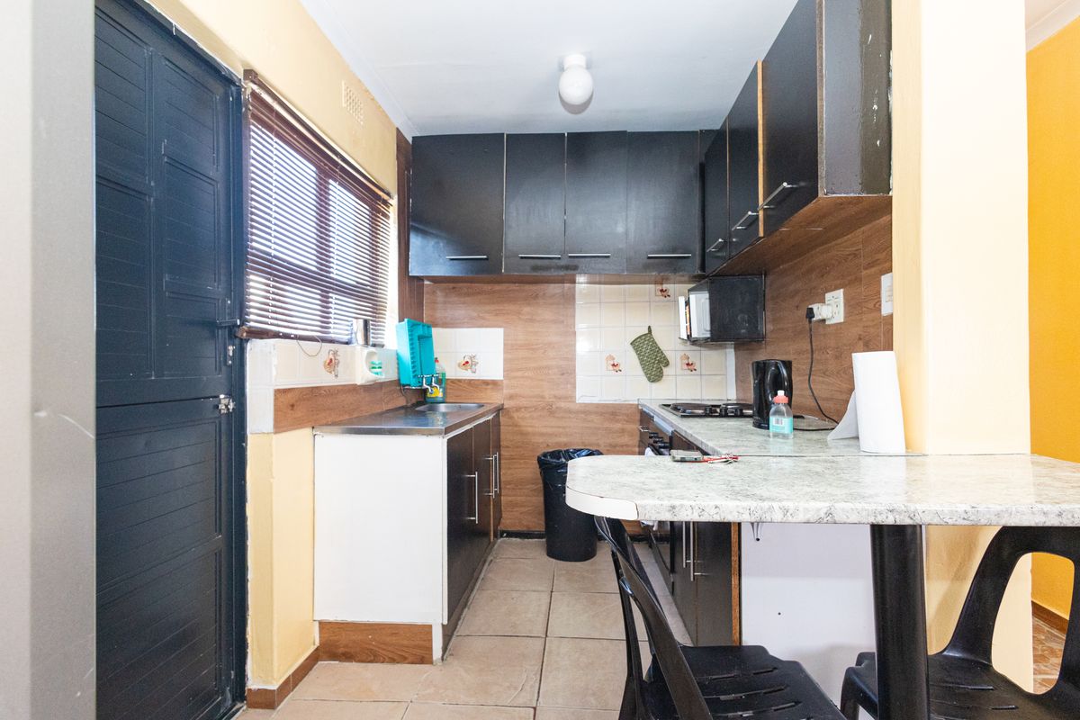 A compact kitchen featuring dark cabinetry, a built-in hob, tiled backsplash, and a breakfast bar area with tiled flooring.