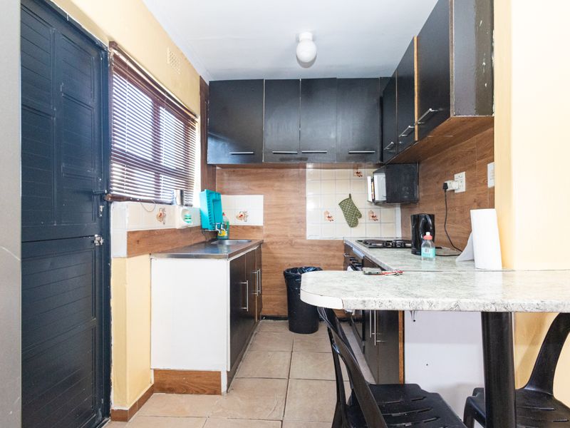 A compact kitchen featuring dark cabinetry, a built-in hob, tiled backsplash, and a breakfast bar area with tiled flooring.