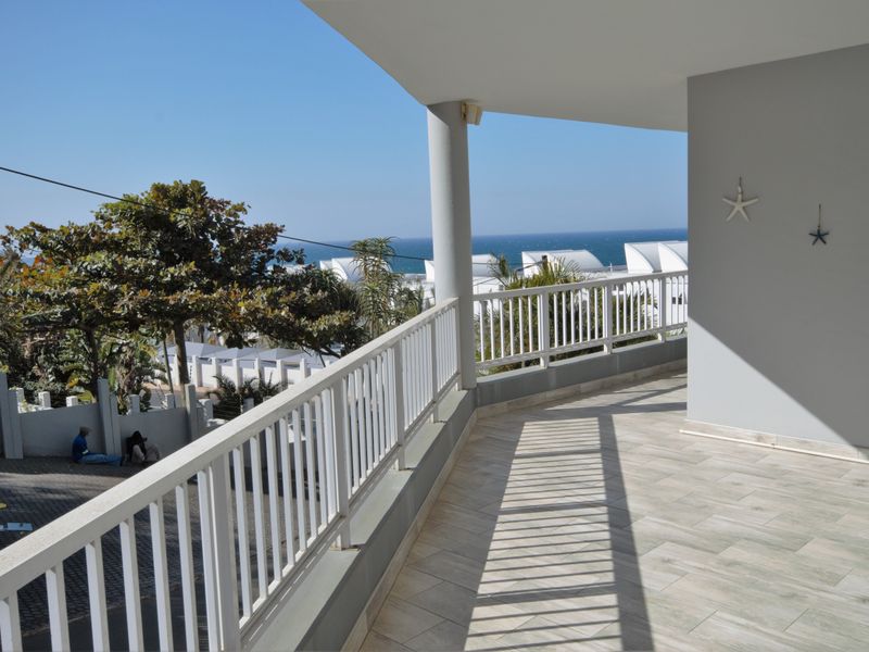 A spacious covered balcony featuring tiled flooring, a white metal balustrade, and scenic coastal views.