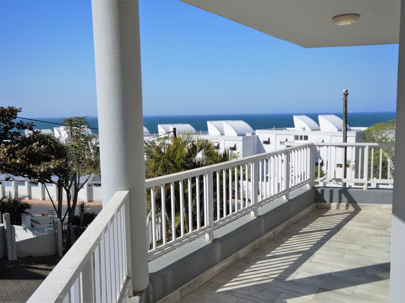 A spacious balcony featuring tiled flooring, a white metal balustrade, and a structural column, offering clear views of the surrounding neighborhood and ocean.
