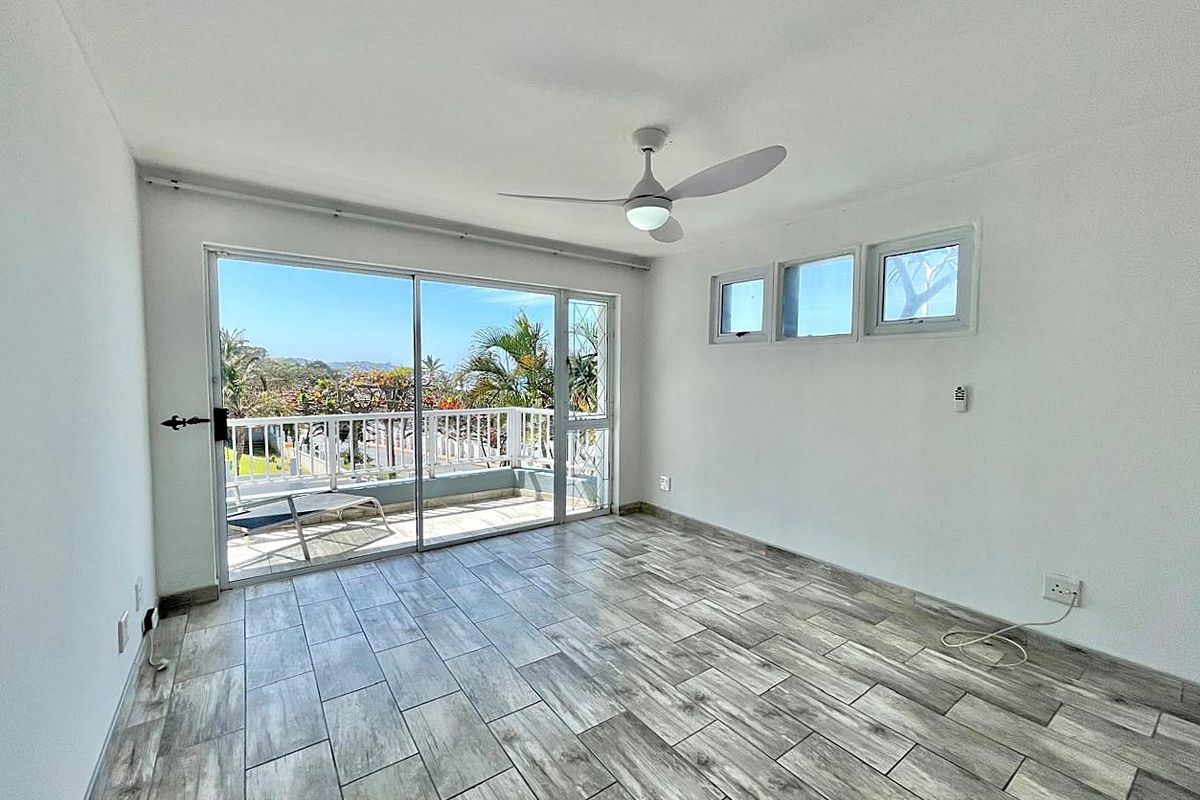 Bright and spacious living area featuring modern wood-look tile flooring, a ceiling fan, and large sliding glass doors opening to a private balcony.