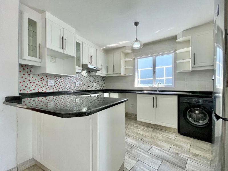 Modern kitchen featuring white cabinetry, granite countertops, a mosaic tile backsplash, and integrated laundry facilities, offering a clean and functional workspace.