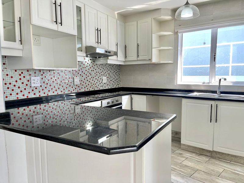 A functional kitchen featuring white cabinetry, dark granite countertops, a mosaic tile backsplash, and built-in appliances, offering a clean and bright workspace.