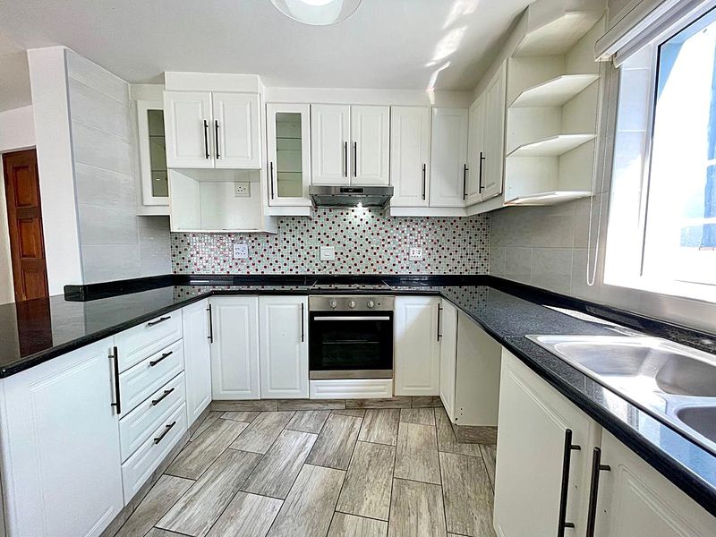 A clean, modern kitchen featuring white cabinetry, black granite countertops, a mosaic tile backsplash, and integrated oven with extractor fan.