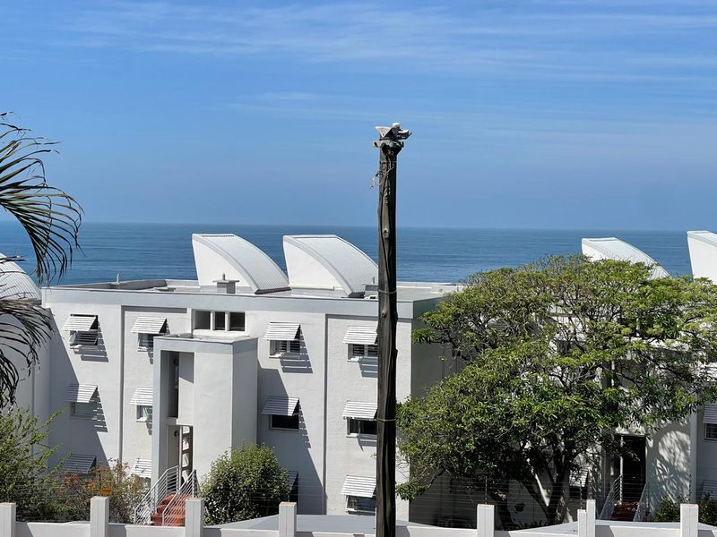 A scenic view of the ocean overlooking the exterior facade of a multi-story apartment complex with distinctive roof features.
